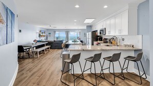 Een moderne keuken met witte kasten, een centraal eiland met barstoelen en uitzicht buiten.