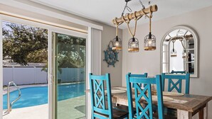 A dining area with a pool view, wooden chairs, and a rustic chandelier.
