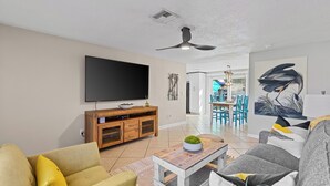 A living room with a flat-screen TV, wooden entertainment unit, and a dining area with chairs and a table.