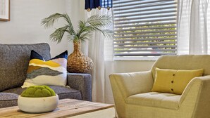 A living room with a grey sofa, a yellow armchair, a wooden coffee table, a white bowl with a green plant, and a large potted plant.
