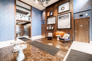 A modern lobby with a marble floor, two seating areas with fluffy chairs, a reception desk, and a large framed artwork on the wall.