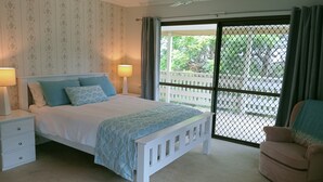 A bedroom with a bed, nightstands, a chair, a ceiling fan, and a view through a screened door. - Spacious, comfortable, Pet Friendly 3-Bed House minutes from the Big Pineapple  (Woombye)