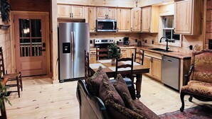 A wooden cabin interior with a kitchen, dining area, and a cozy seating area.