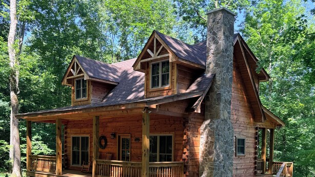 A log cabin with a porch, stone chimney, and a staircase leading to the upper level.
