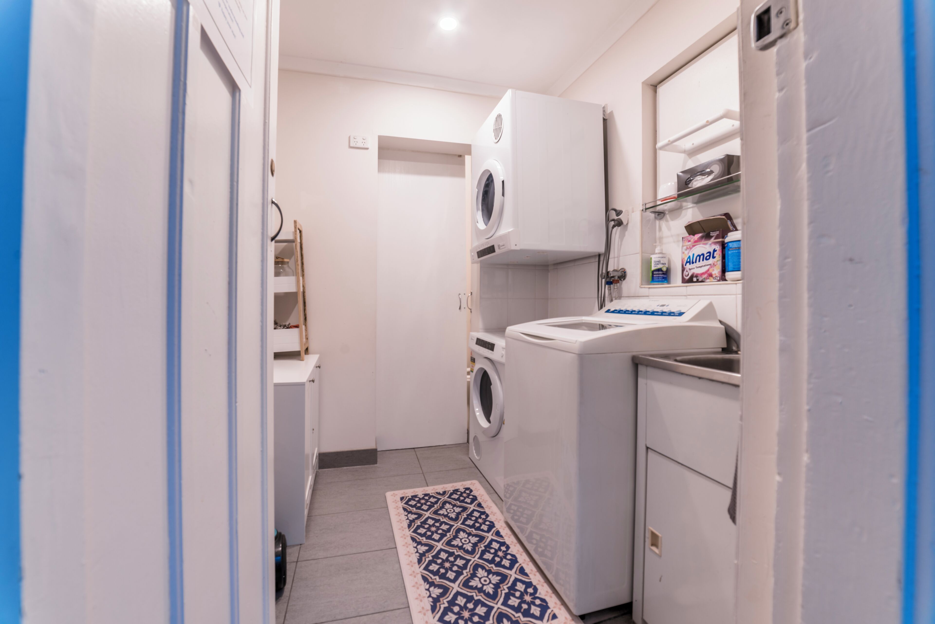 A compact laundry room with a washing machine, dryer, and a small cabinet with a shelf.