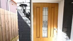 A wooden door with a glass panel and a metal handle, adjacent to a black brick wall and a wooden fence. - 3BR Glen Iris Gem – Sleeps 7, Near Train & Freeway with WiFi and AC (Glen Iris)