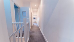 A hallway with a carpeted floor, white walls, and a door leading to another room. - 3BR Glen Iris Gem – Sleeps 7, Near Train & Freeway with WiFi and AC (Glen Iris)