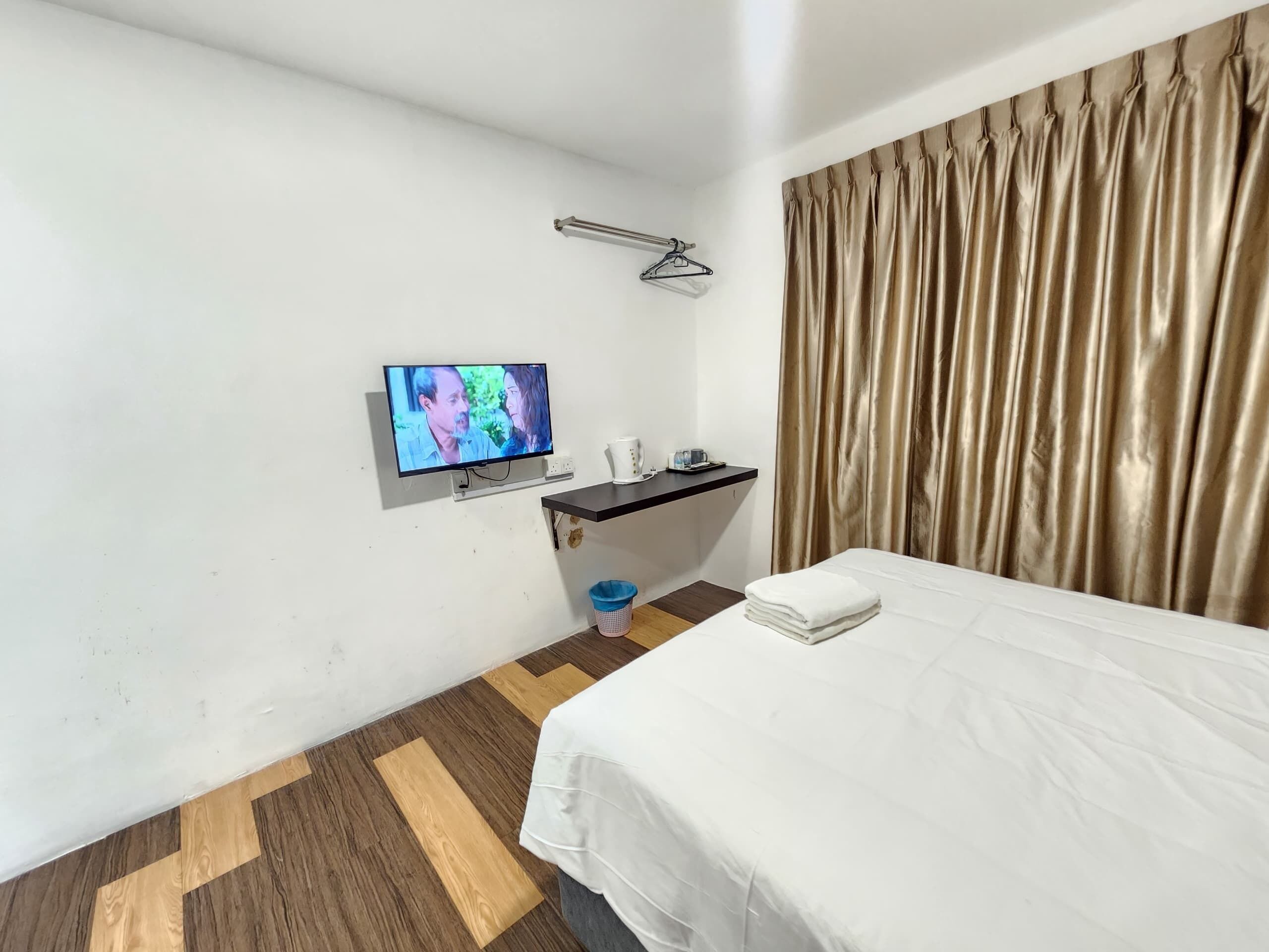 Habitación de hotel con cama, televisión montada en la pared, escritorio pequeño con espejo, lavamanos y ventana con cortinas.