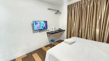 Habitación de hotel con cama, televisión montada en la pared, escritorio pequeño con espejo, lavamanos y ventana con cortinas.