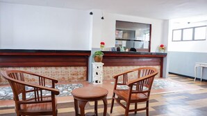Een receptiegedeelte met een balie, twee houten stoelen, een kleine tafel en een potplant.