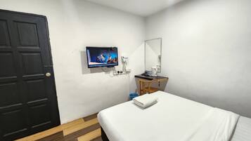 A hotel room with a bed, a TV mounted on the wall, a small wooden table with a kettle, and a mirror.
