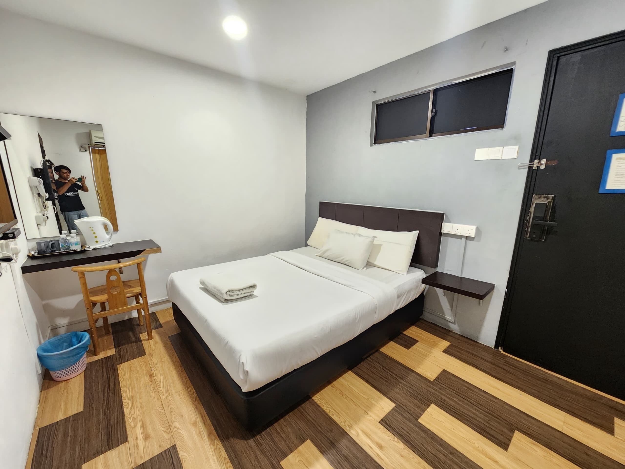 Un dormitorio ordenado con cama, escritorio, silla y una pequeña zona de kitchenette.