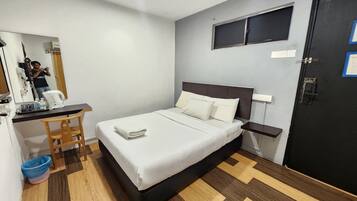 Un dormitorio ordenado con cama, escritorio, silla y una pequeña zona de kitchenette.
