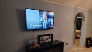 Un salon doté d’un téléviseur à écran plat fixé au mur, d’un meuble de rangement en bois foncé en dessous, et d’un couloir menant à une autre pièce.