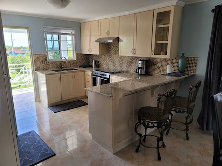 A kitchen with beige cabinets, a stove, a coffee maker, and a dining area with two chairs.