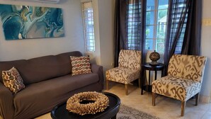 Un salon avec un canapé marron, des fauteuils à motifs, une table basse noire agrémentée d’un élément décoratif, et un grand tableau abstrait accroché au mur.