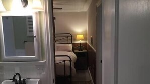 A narrow hallway leading to a bedroom with a bed, a nightstand with a lamp, and a bathroom with a sink and mirror. - 1st Floor - 1 mile from San Moritz Lodge (Crestline)