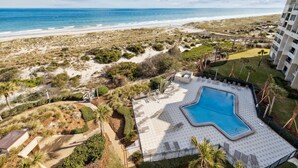Et poolområde med stjerneformet design, omgivet af en anlagt have og udsigt til stranden.