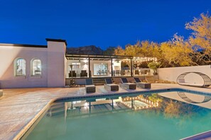 A pool area with lounge chairs, a covered patio, and a mountain backdrop.