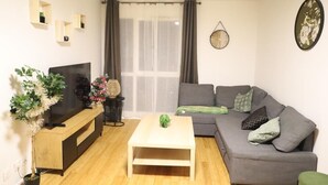 A living room with a TV, sofa, coffee table, and plants.