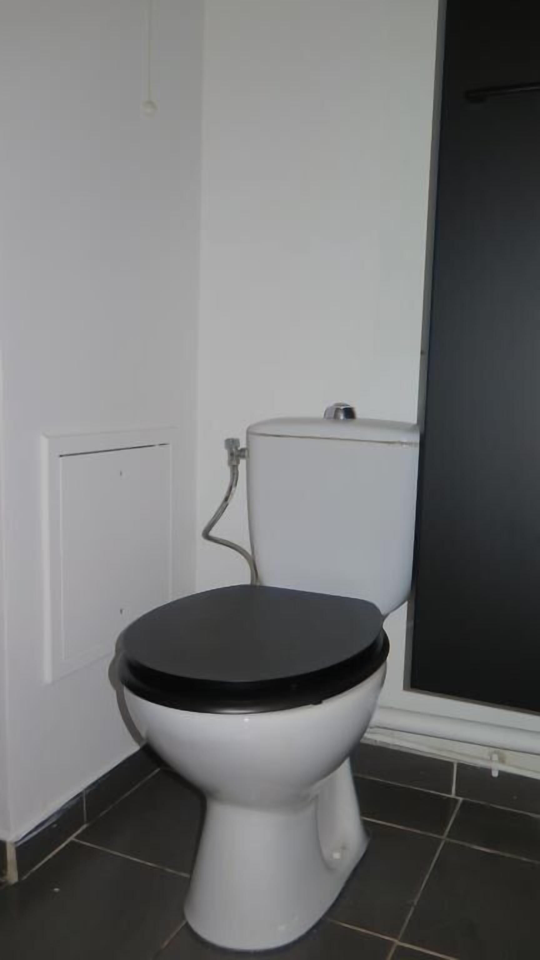 A white toilet with a black seat in a bathroom with tiled flooring.