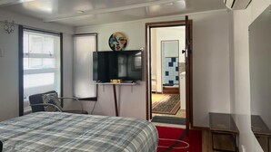 Ein Schlafzimmer mit einem Bett, einem an der Wand montierten Fernseher, einem Schreibtisch und einer Tür zu einem Badezimmer.