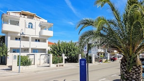 Un immeuble à plusieurs étages doté de balcons, un ciel d’un bleu éclatant et un palmier au premier plan.