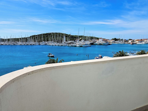 A marina with numerous sailboats docked, a small motorboat in the water, and a hillside in the background.