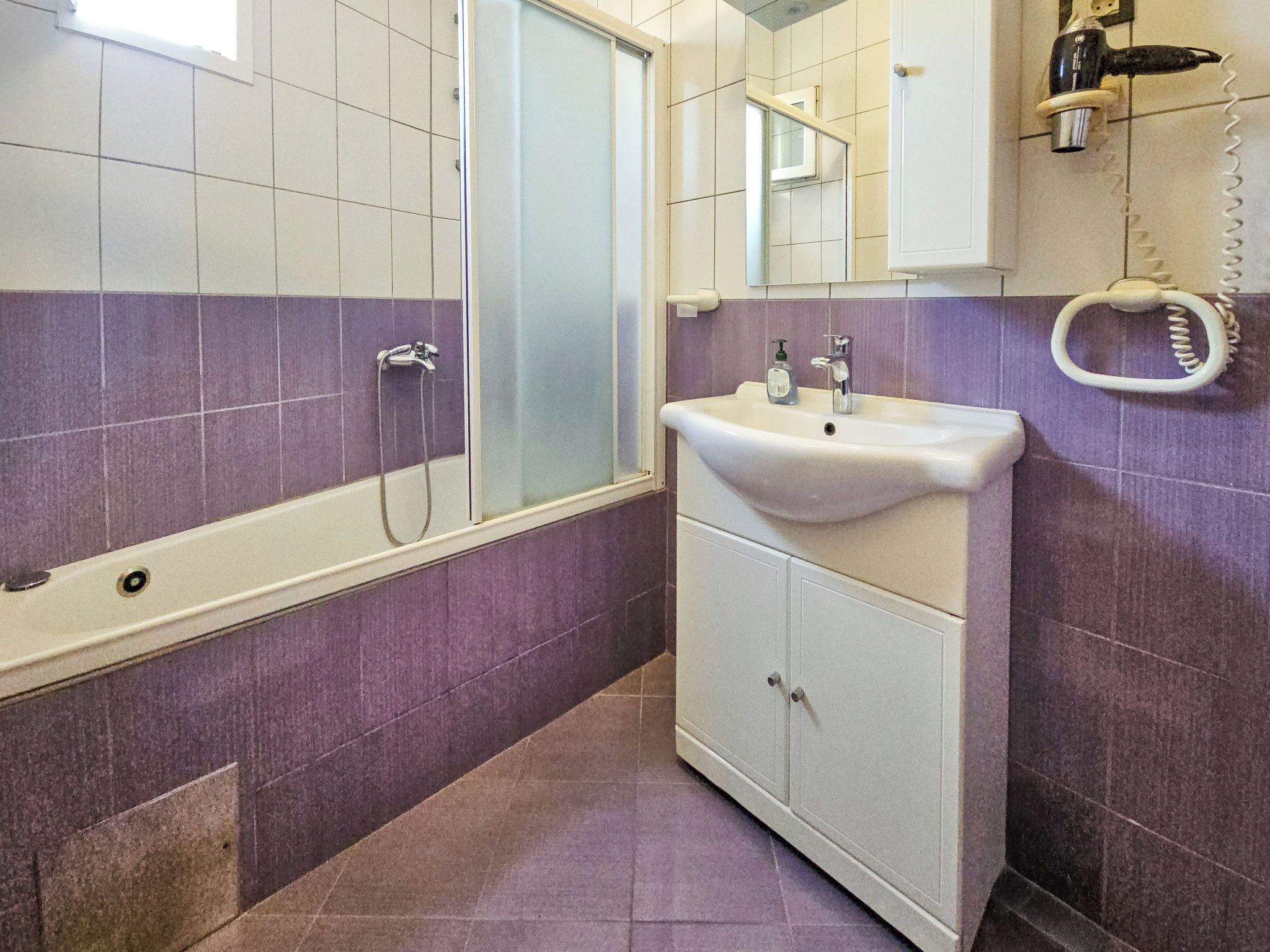 A bathroom with a bathtub, a sink, a mirror, and a hairdryer on the wall.