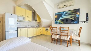A compact hotel room with a bed, a dining table with chairs, a kitchenette, and a TV mounted on the wall. - Apartment Miline by Interhome (Rogoznica)