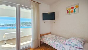 Un dormitorio con piso de madera, una cama con ropa de cama floral, un televisor en la pared y un balcón con mesa y sillas.