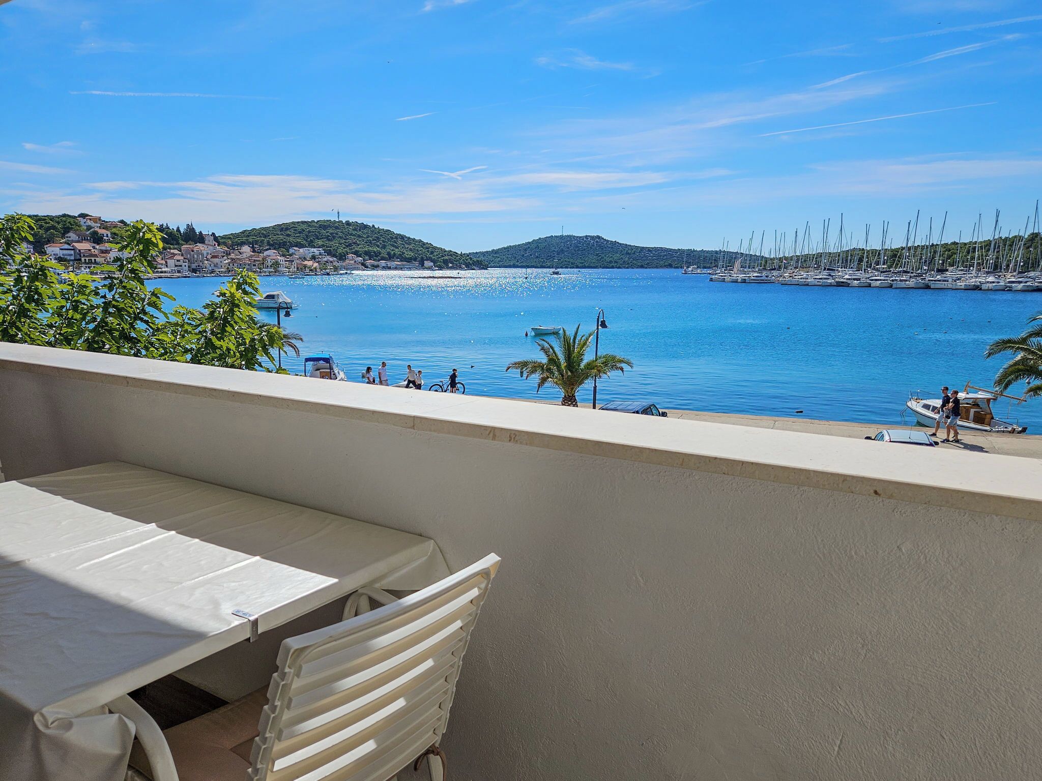 A balcony with a table and chairs overlooking a marina with boats and a coastal town.