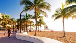 A beach promenade lined with palm trees, a lifeguard tower, and a sandy beach. - Waterfront | Boat Rental | Heated Pool | Games Room | Sleeps 8 (Lighthouse Point)