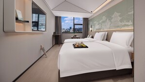 Habitación de hotel moderna con una cama grande, una mesita con una bandeja de fruta, vista a la ciudad por la ventana y un elemento decorativo en la pared.