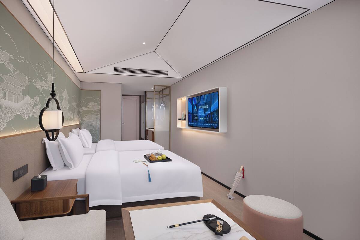 A modern hotel room with a large bed, a desk with a lamp, a flat-screen TV, and a decorative wall mural.