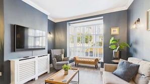 A living room with a TV, sofa, armchair, bench, and a potted plant. - Simeon Sands Coastal Escape (Ryde)