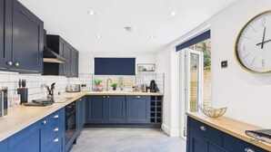 A modern kitchen with dark blue cabinets, a wooden countertop, a built-in oven, and a large wall clock. - Simeon Sands Coastal Escape (Ryde)