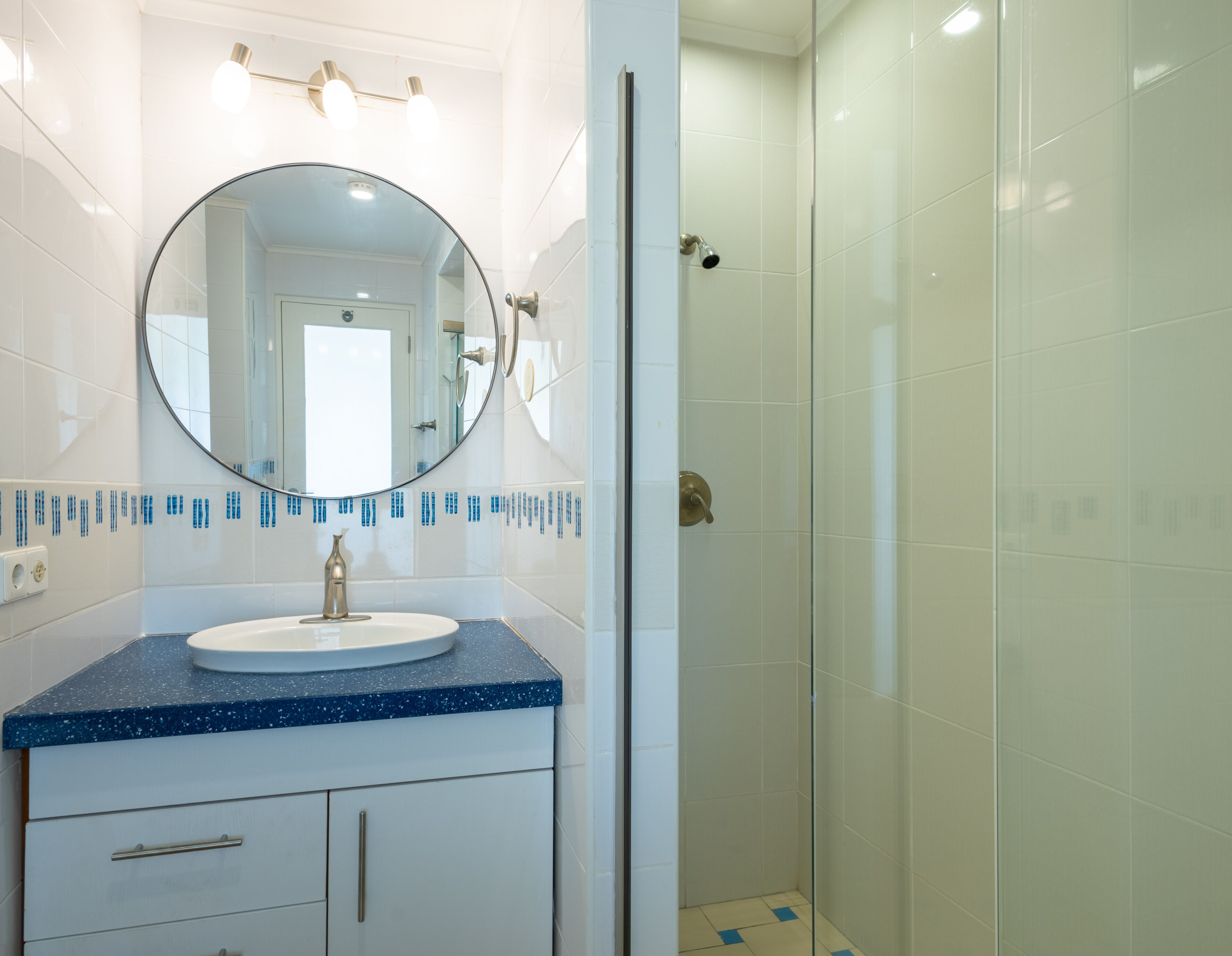 A bathroom with a round mirror, a sink with a blue countertop, and a shower area.