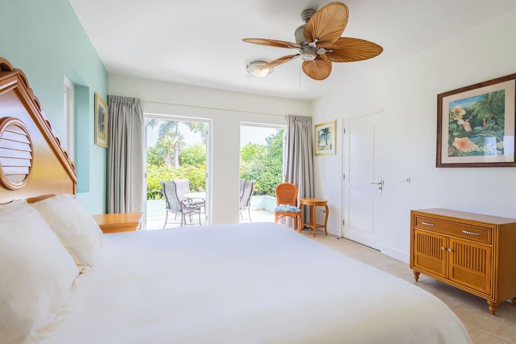 A hotel room with a large bed, a ceiling fan, a wooden dresser, and a view of the outdoors.