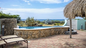 Una piscina con una parete in pietra, un tetto di paglia e vista sull'oceano.