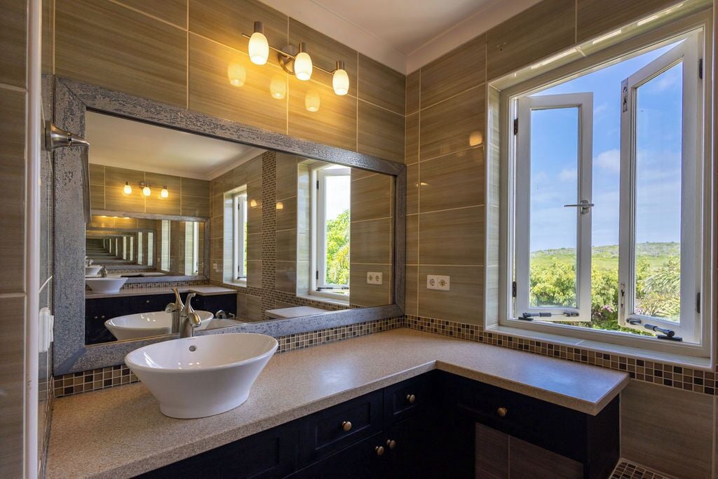 A bathroom with a large mirror, two sinks, and a window with a view of greenery.