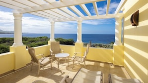 Un balcone con vista sull'oceano, colonne bianche e sedie color beige.