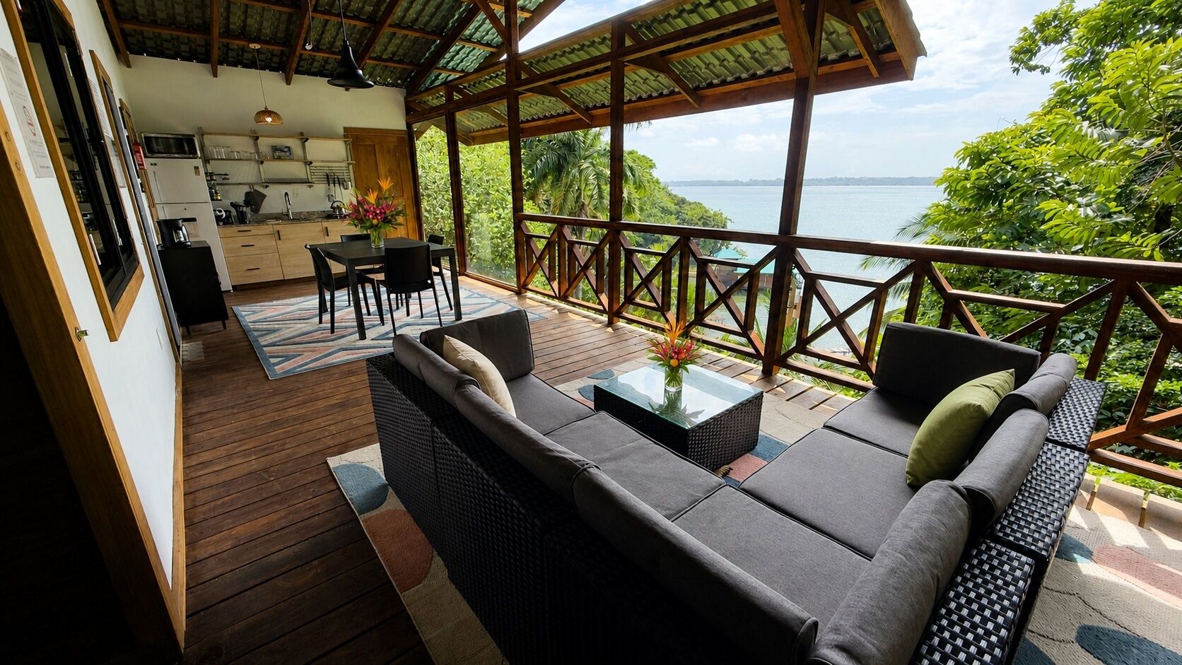 A wooden deck with a sofa and table, a kitchen area, and a view of the sea.