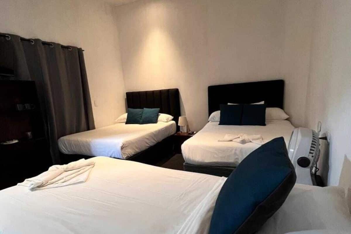 Hotellihuone, jossa on kaksi erillistä sänkyä, joissa kummassakin on pääty ja tyyny, yöpöytä lampun kanssa sekä suuri sänky, jossa on tyyny.