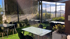 Un área de estar al aire libre con mesas y sillas, un césped y vistas del cielo y el paisaje lejano a través de amplias ventanas.