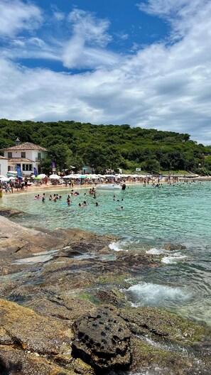 Uma praia com águas turquesa cristalinas, margem rochosa e muitas pessoas aproveitando o mar.