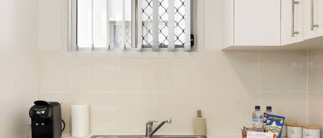 A kitchen with a coffee maker, a sink, a window with bars, and a breakfast tray with cereal and milk.