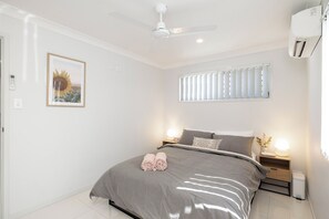 A bedroom with a bed, a ceiling fan, a nightstand with a lamp, and a window with blinds. - Smart Suites Self Check-in Apartments - 14 Freney (Rocklea)