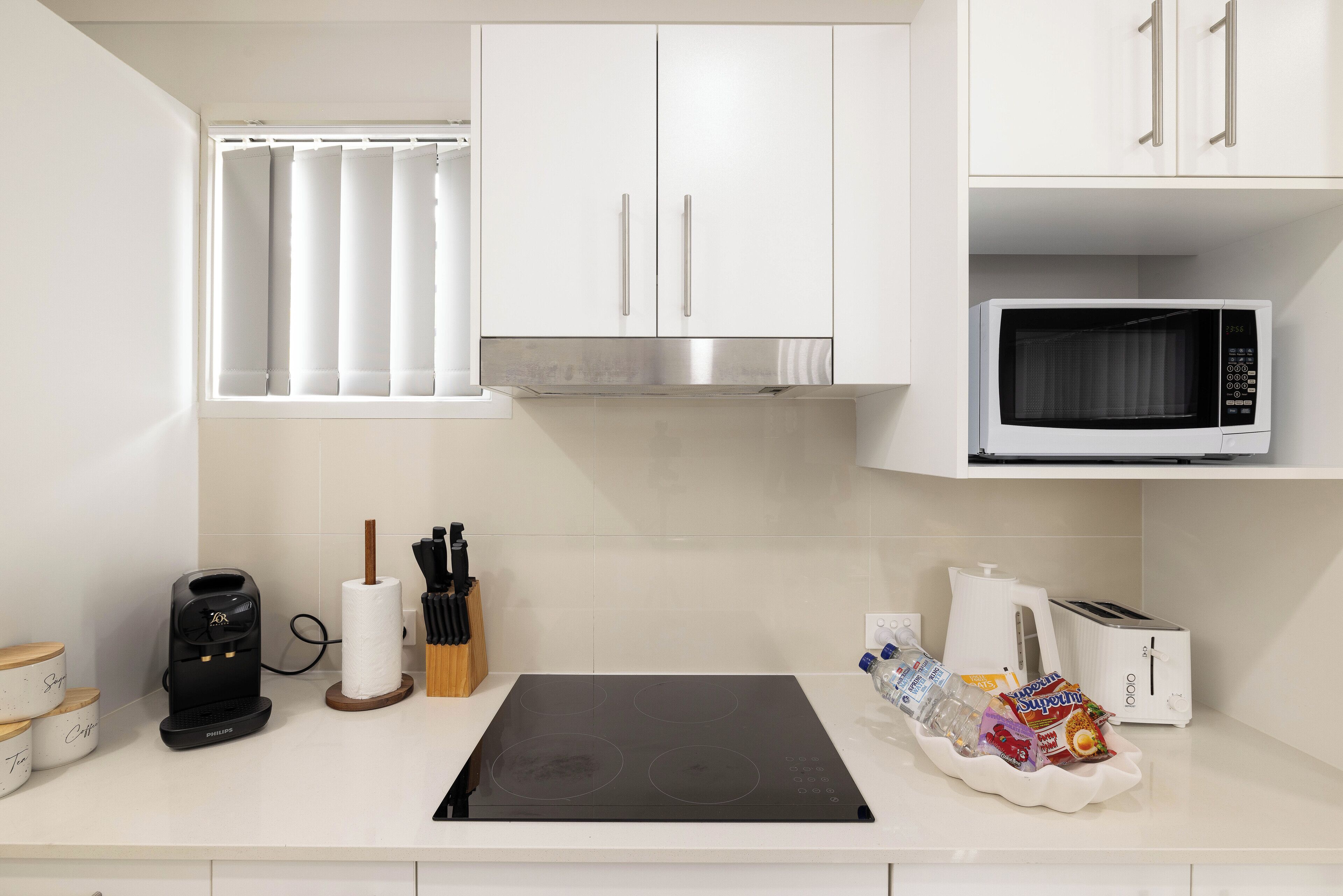 A modern kitchen with white cabinets, a built-in microwave, a coffee maker, and a toaster.