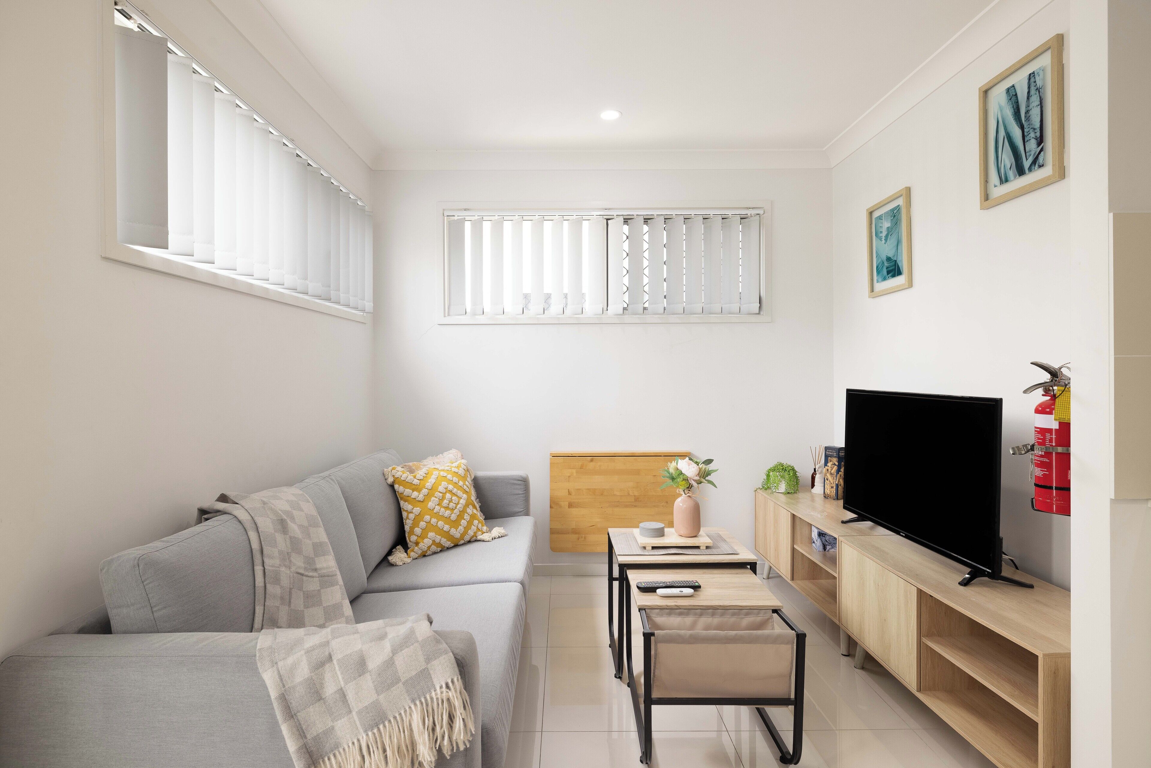 A modern living room with a grey sofa, a small wooden table, a TV, and a bookshelf.